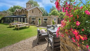 Une maison en pierre dotée d’une véranda, d’un espace extérieur aménagé et d’un jardin où poussent des fleurs roses.