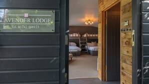Une pièce avec des lits superposés, une échelle et une petite table. Il y a une pancarte sur la porte indiquant « Lavender Lodge » et un numéro de téléphone.