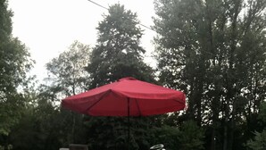Ein Tisch mit einer Champagnerflasche, zwei Gläsern und einer Oliven-Schale. Im Hintergrund sind ein roter Sonnenschirm und Gartenmöbel zu sehen.