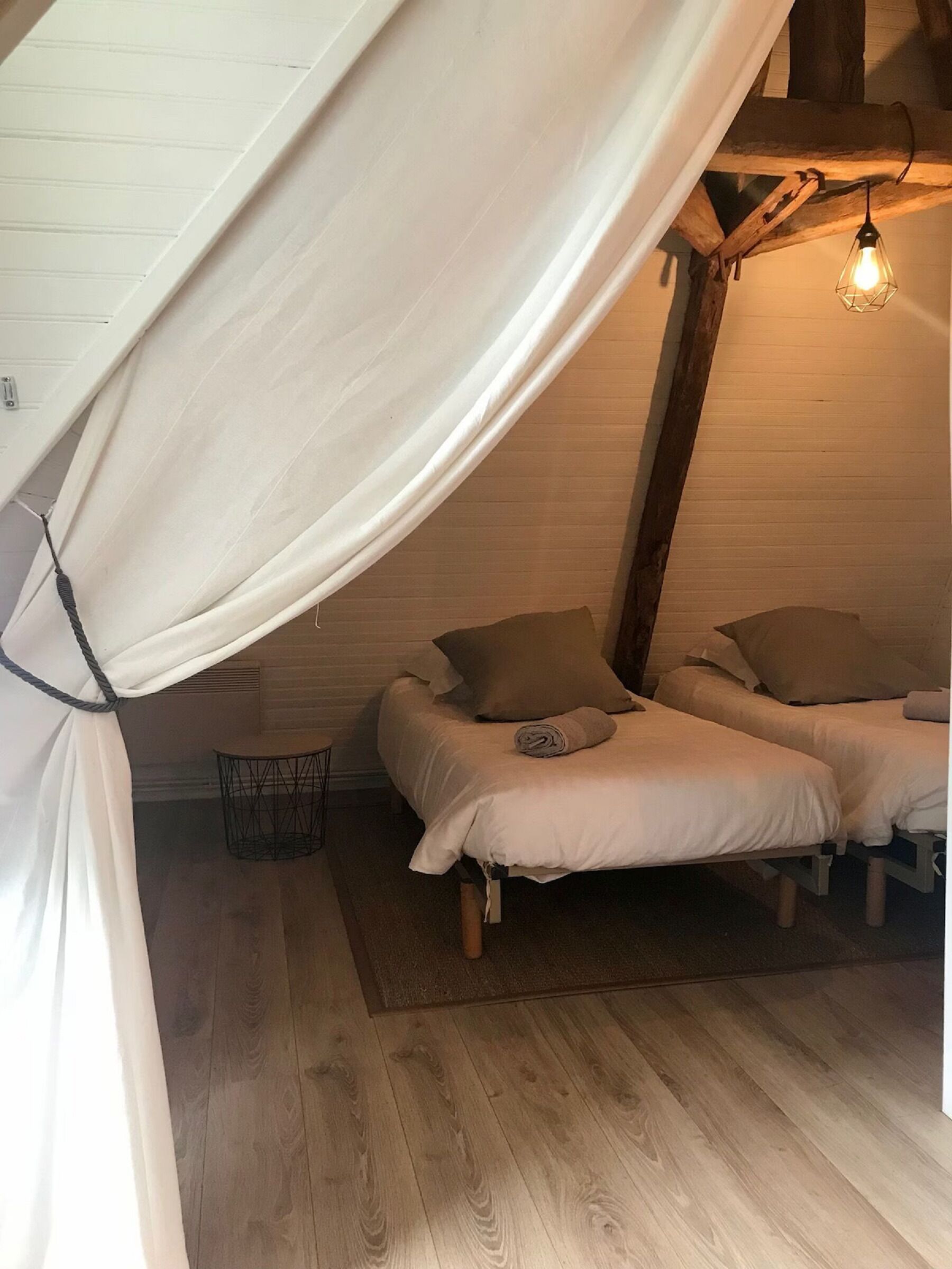 Et hyggeligt soveværelse på loftet med to senge, en hængende lampe og en lille skraldespand.