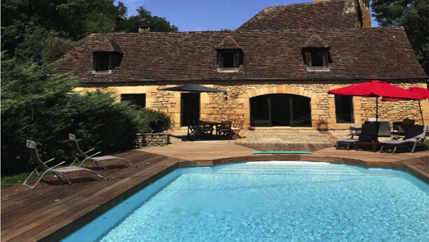 Ein Steinhaus mit Schwimmbad, Sitzgelegenheiten im Freien und einem roten Sonnenschirm.