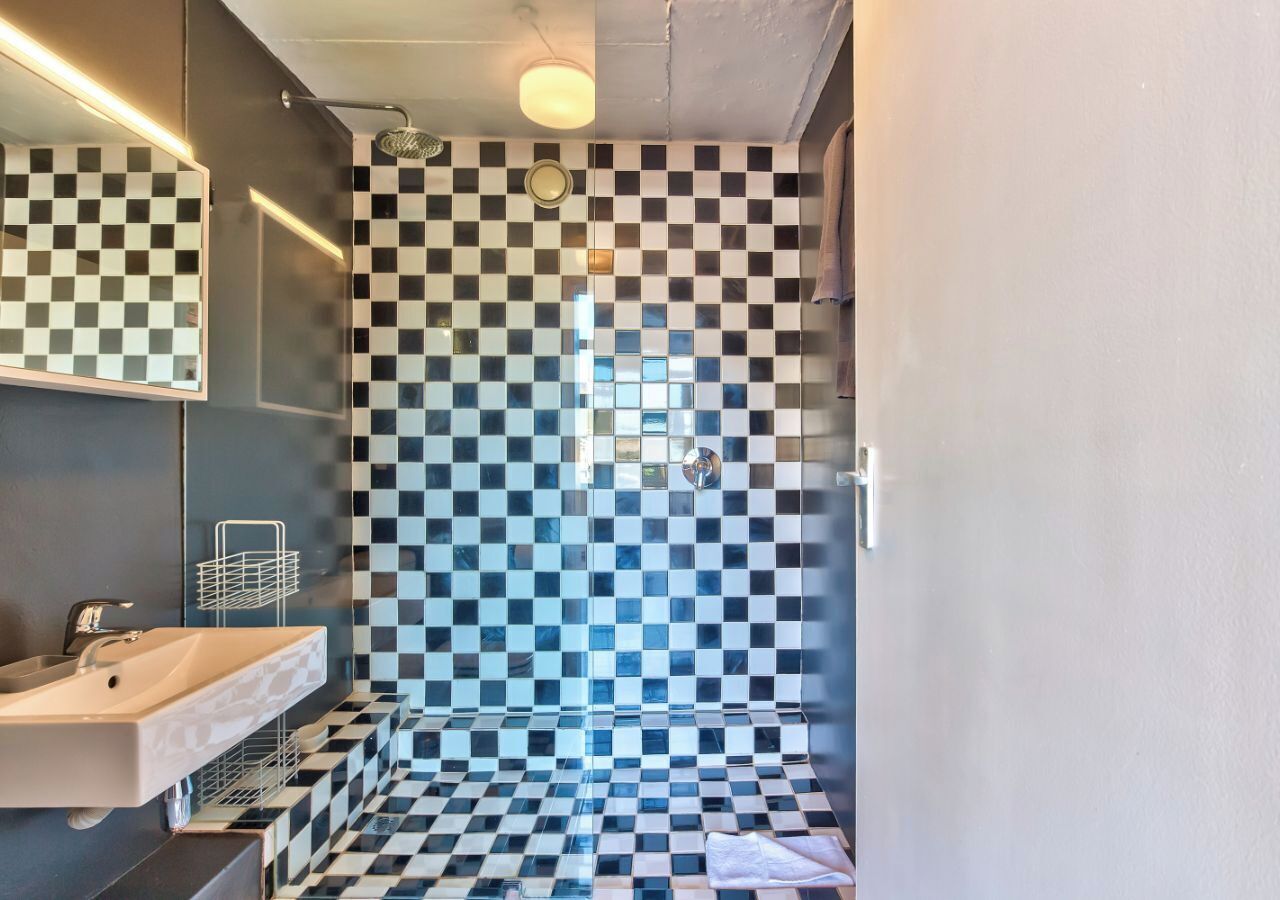 Un baño con pared de baldosas a cuadros, un lavamanos y una ducha.