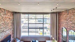 A modern room with a large window, brick walls, a sofa, and a table with a vase. - West Side Studios Mountain View Loft (Cape Town)