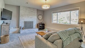A living room with a fireplace, a sofa, a coffee table, and a large window. - Family-Friendly 5BR Retreat – Hot Tub & Game Room (Gresham)