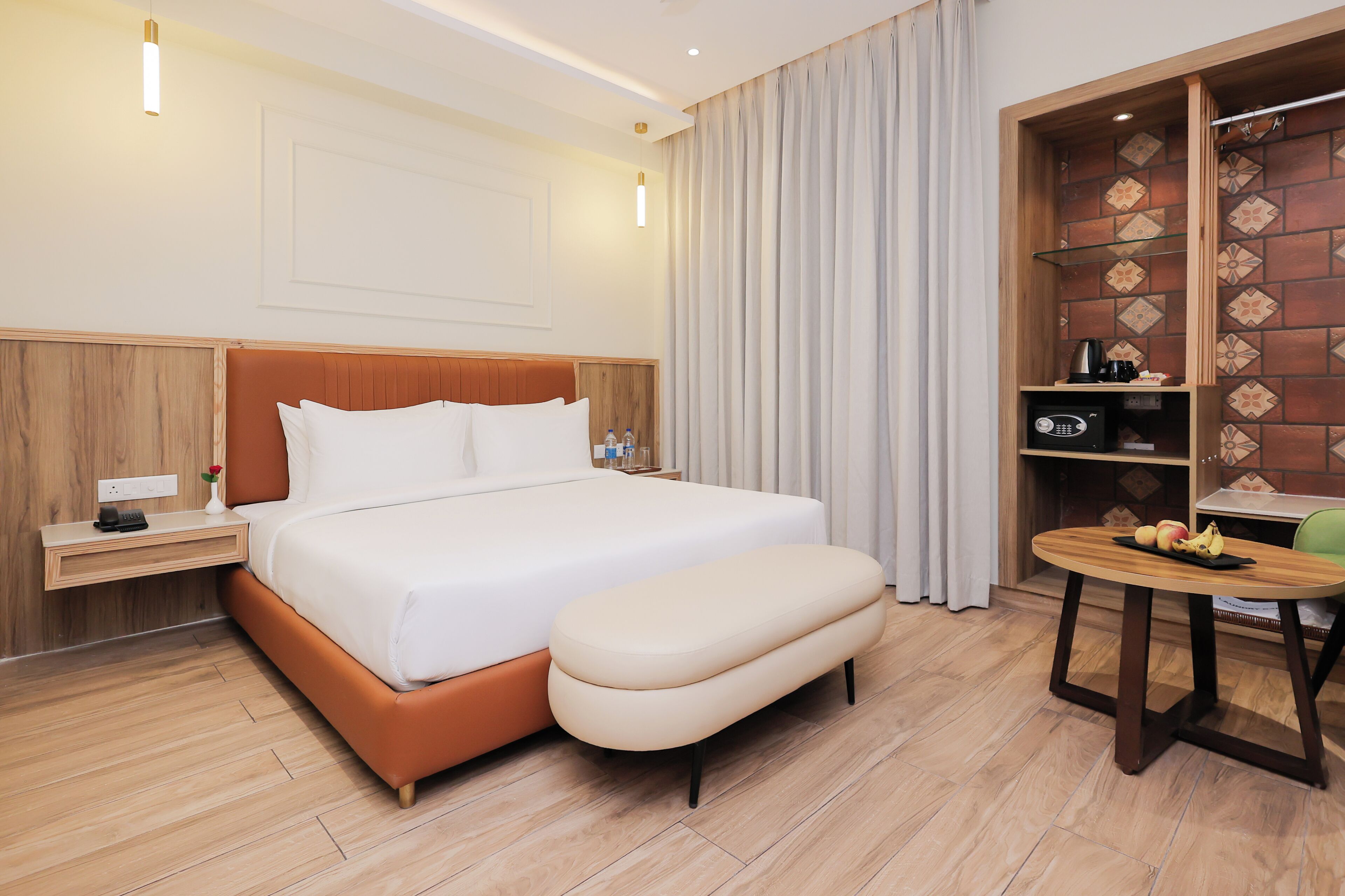 A hotel room with a large bed, a wooden nightstand, a small table with fruit, and a brick-patterned wall.