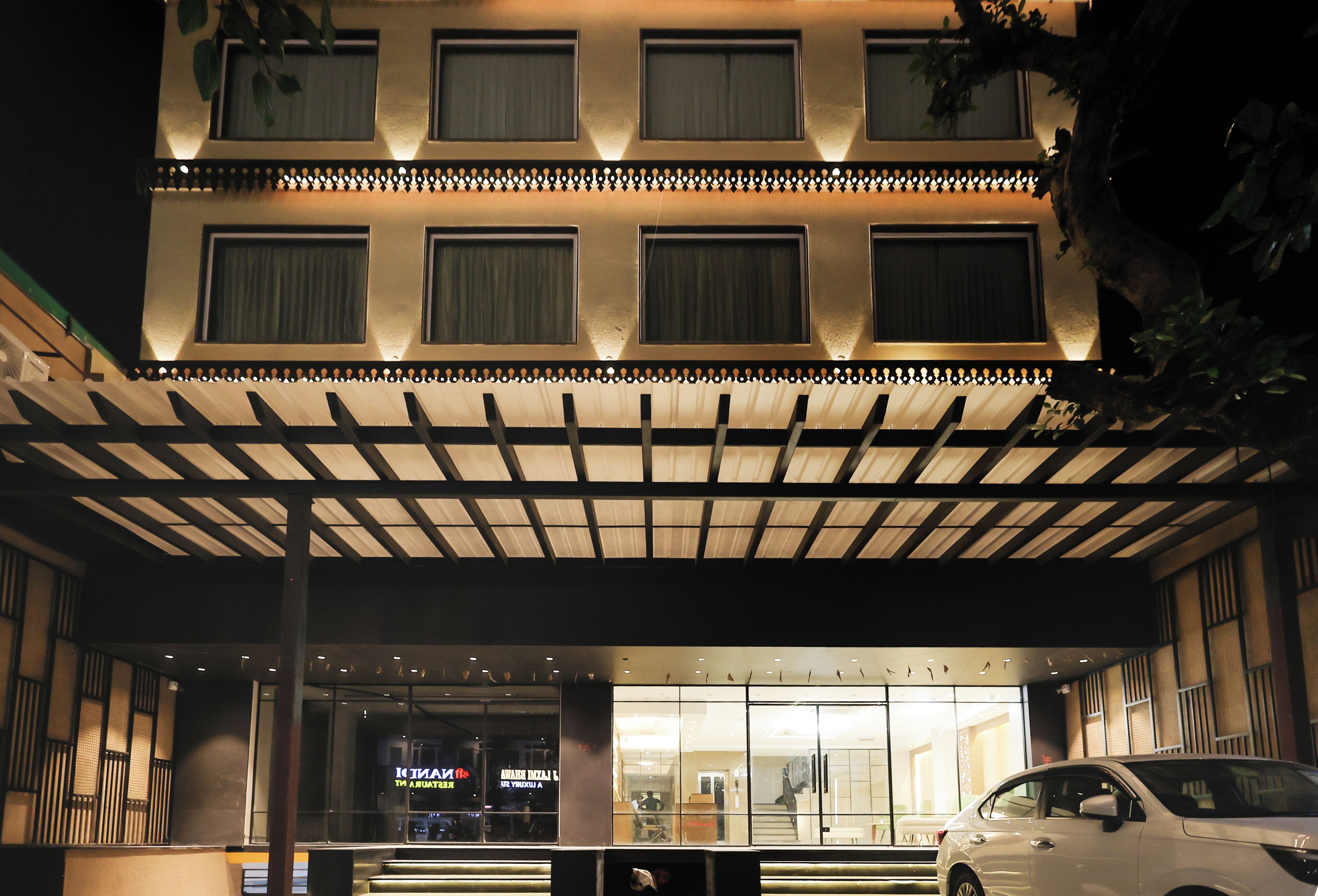 Un hotel de varios pisos con un acceso cubierto y un coche estacionado en la entrada.