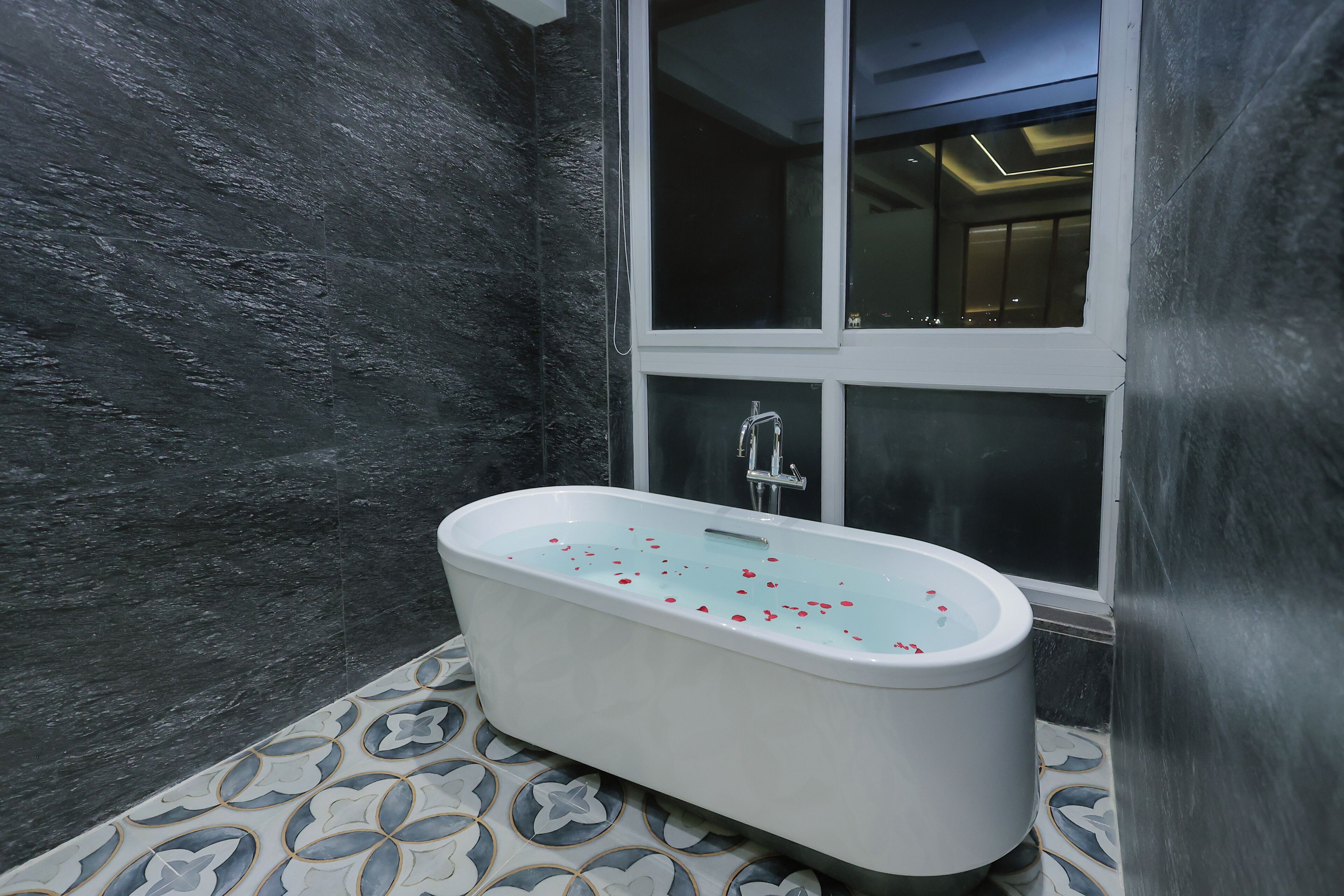 A modern bathroom with a freestanding bathtub, a large window, and patterned floor tiles.