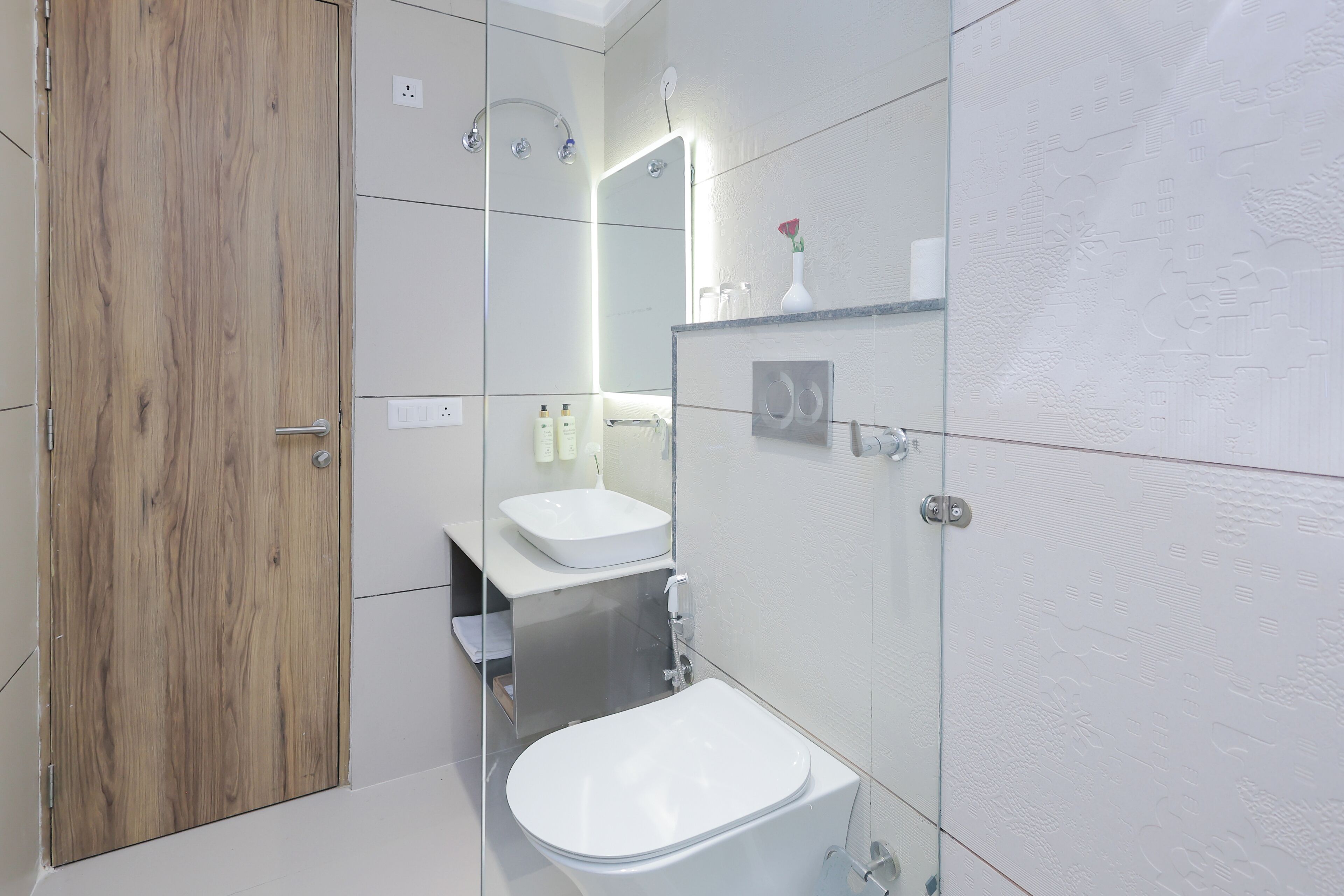 A modern bathroom with a wooden door, a white sink, a mirror, and a toilet.
