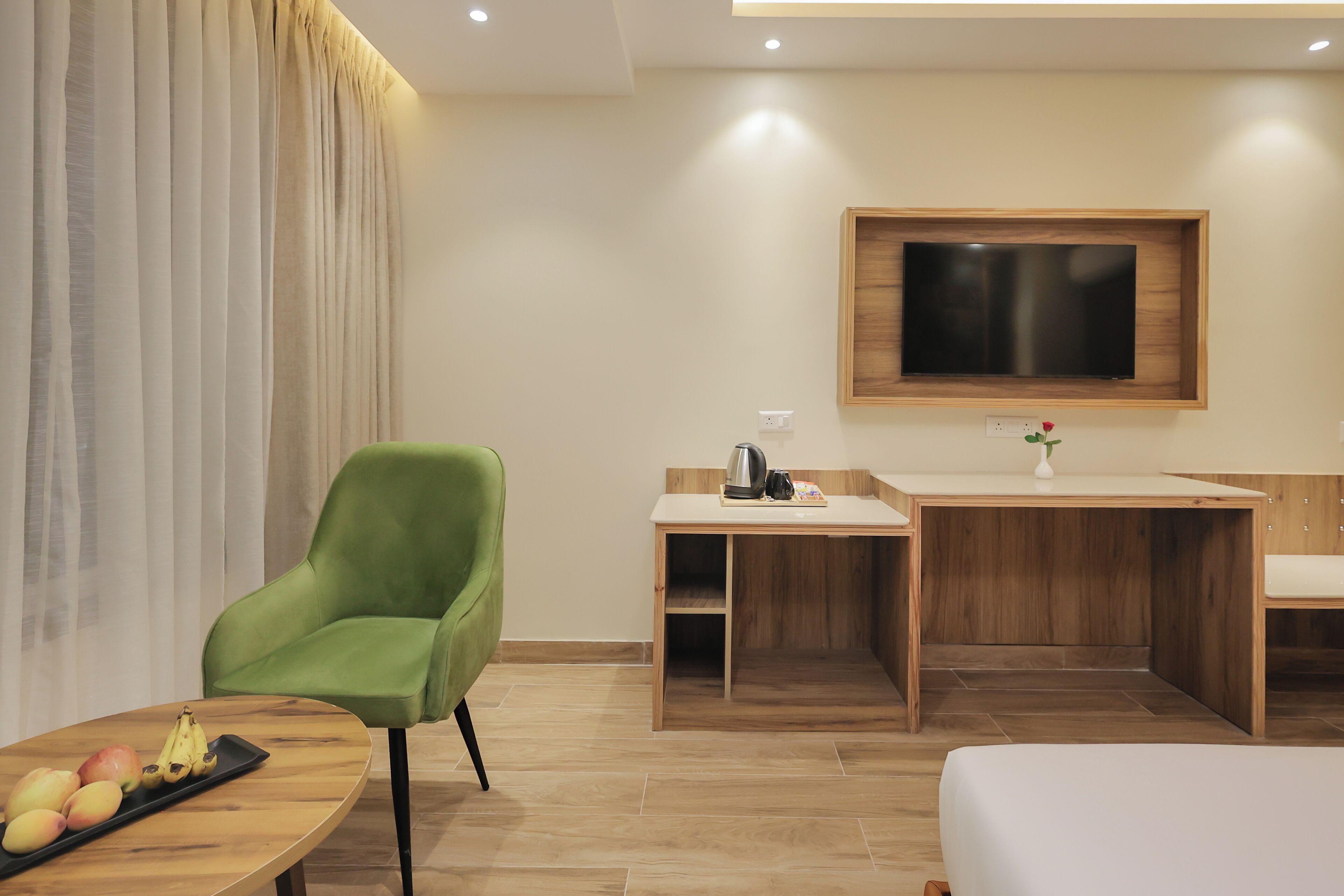 A modern hotel room with a green armchair, a wooden desk, a flat-screen TV, and a bed.
