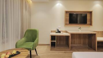 Una habitación de hotel moderna con un sillón verde, un escritorio de madera, un televisor de pantalla plana y una cama.