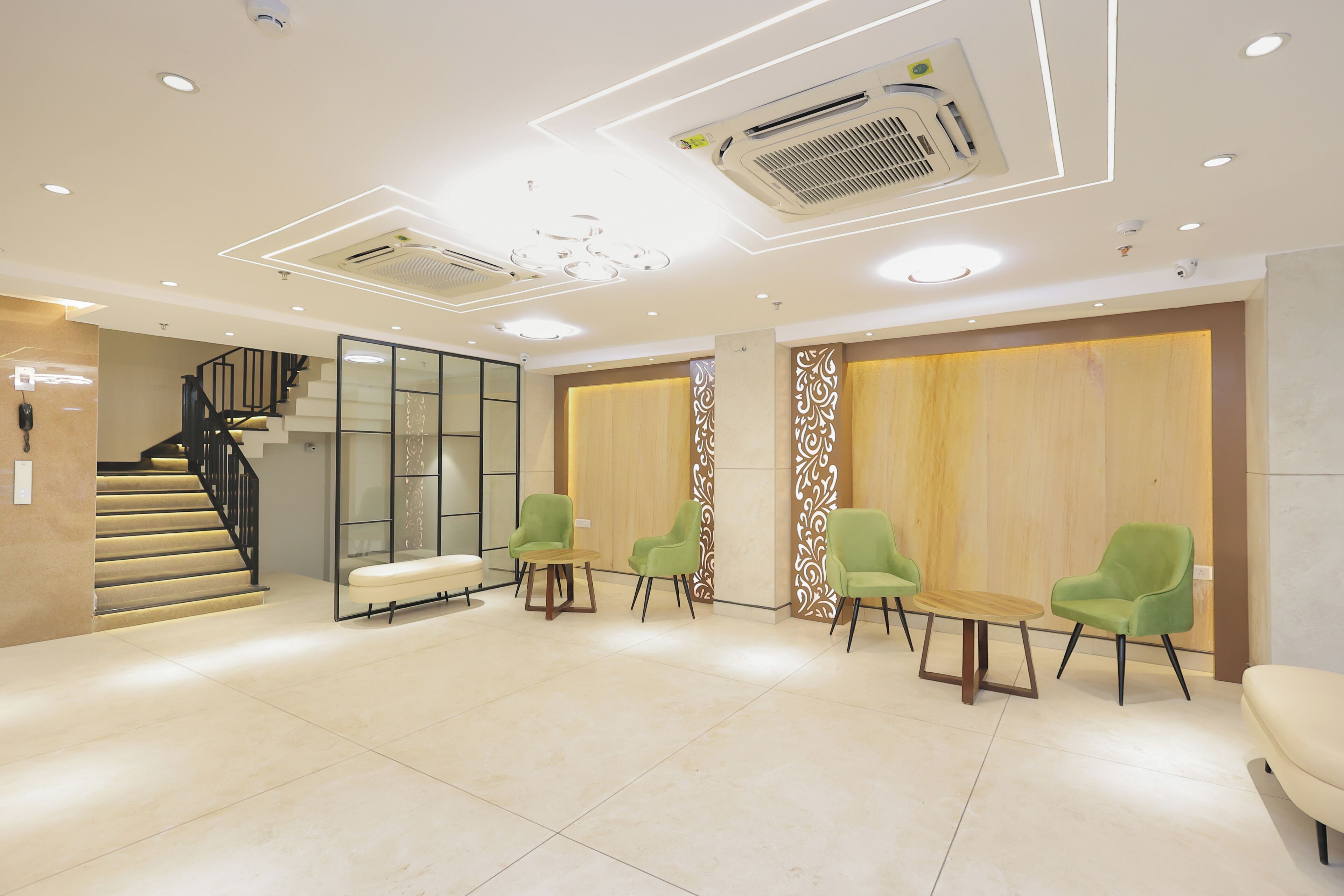 Un vestíbulo moderno con una escalera, sillas verdes y una mesa de recepción.