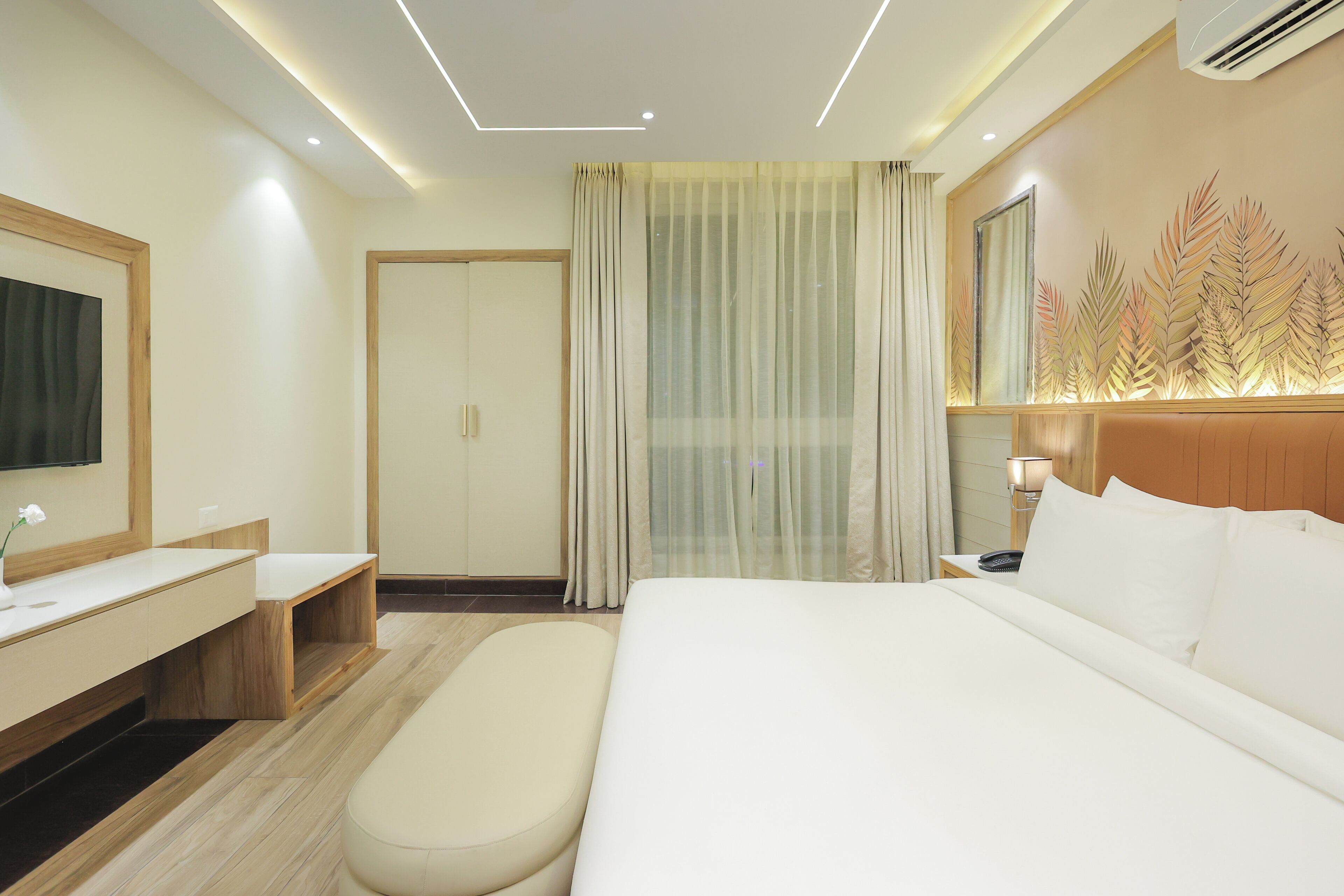 A hotel room with a large bed, a bedside table, a mirror, a TV, and a window with curtains.