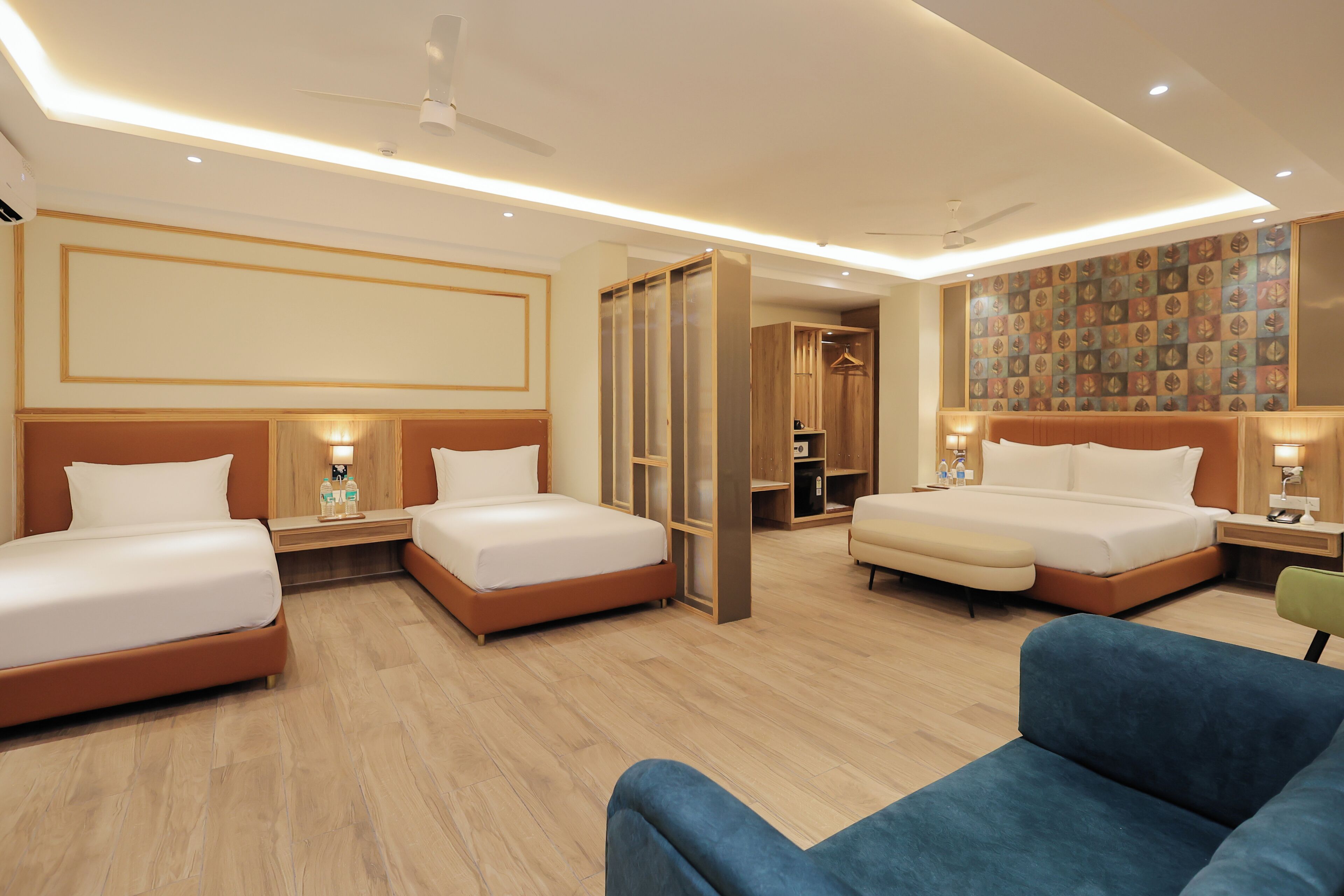 A hotel room with two beds, a blue armchair, wooden flooring, and a wall with a patterned design.