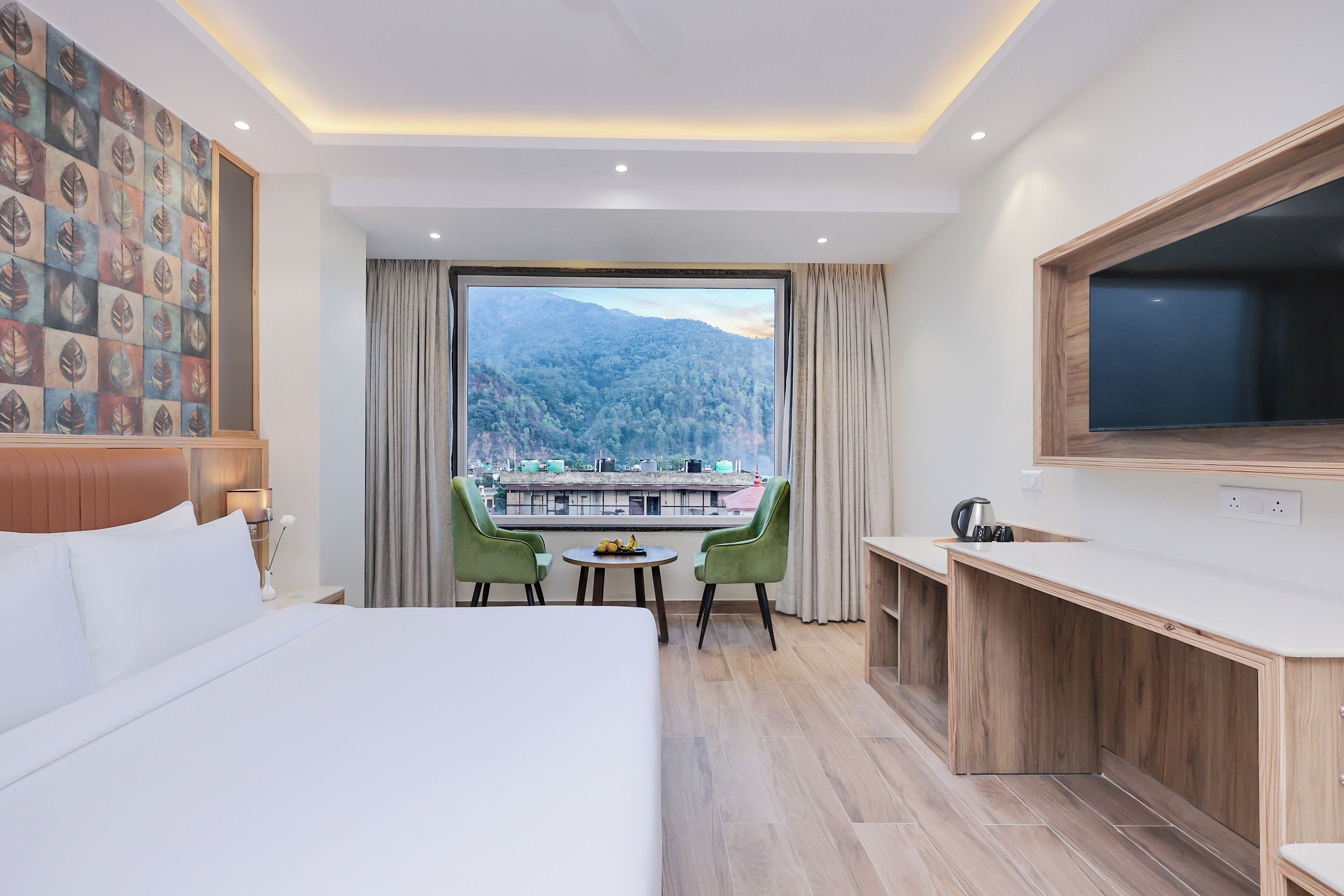 Ein Hotelzimmer mit einem großen Bett, einem Schreibtisch mit Fernseher, Blick auf einen Berg und einem Essbereich mit Stühlen.