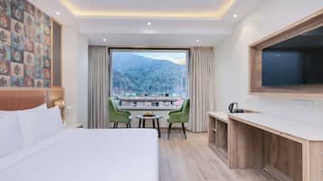 Ein Hotelzimmer mit einem großen Bett, einem Schreibtisch mit Fernseher, Blick auf einen Berg und einem Essbereich mit Stühlen.