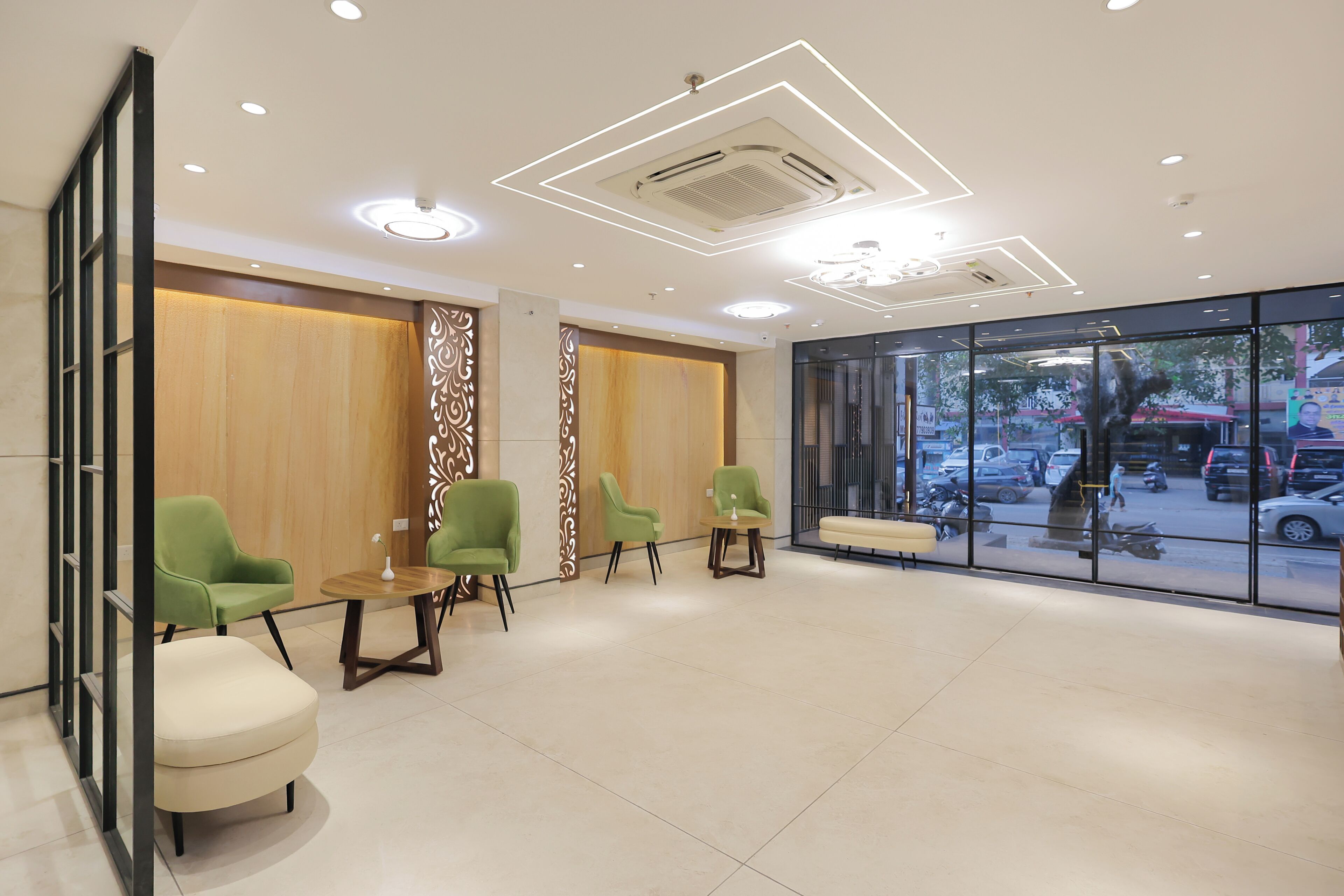 A modern waiting area with green chairs, a wooden partition, and a large window offering a view of the street.