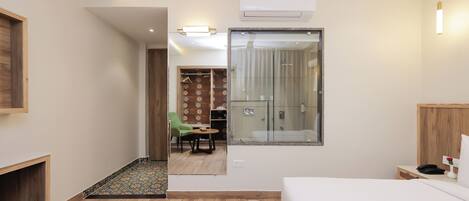 A modern hotel room with a large bed, a small table, a chair, and a glass shower enclosure.