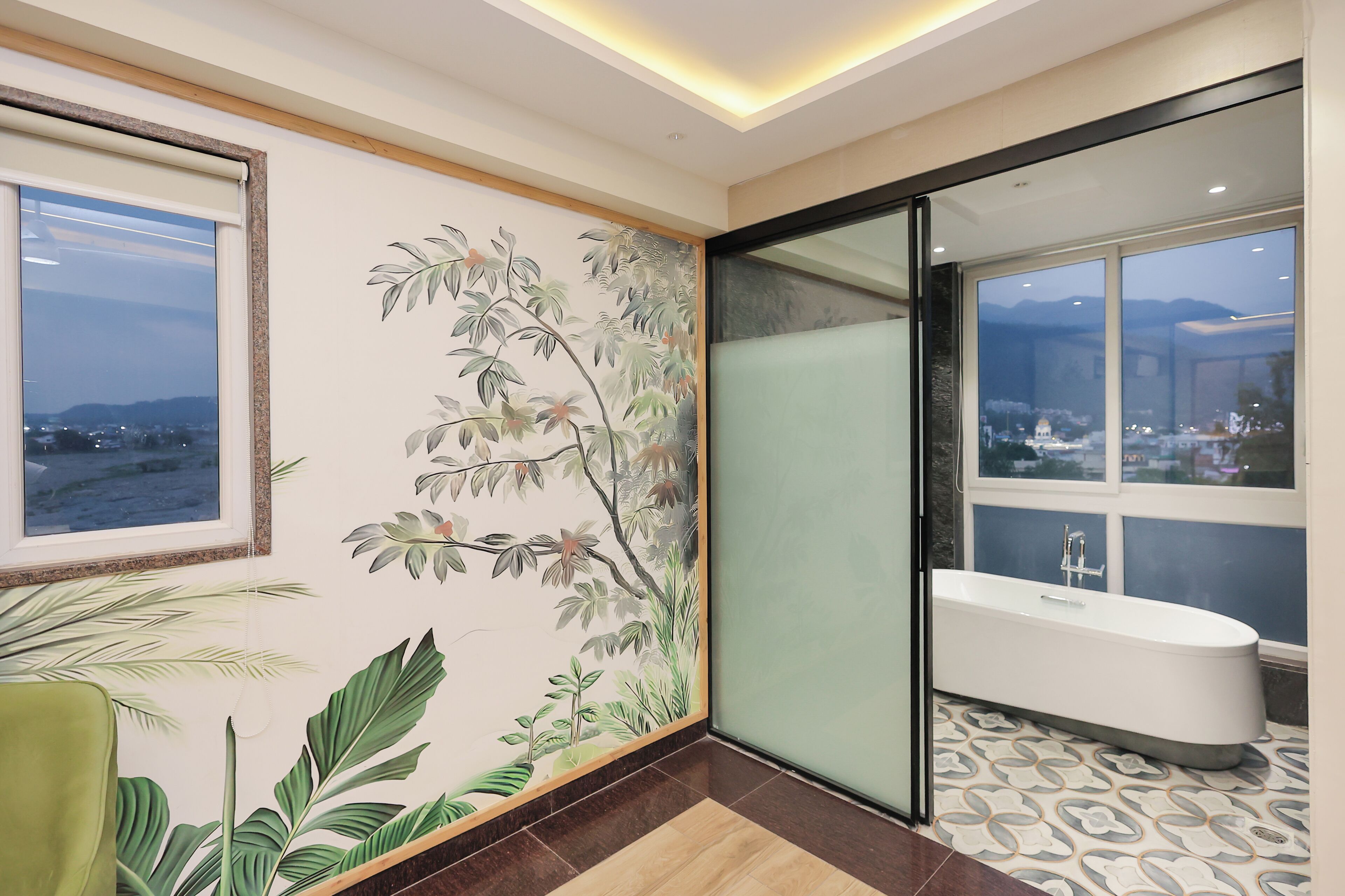 A modern bathroom with a bathtub, a large window with a view of a cityscape, and a decorative wall mural.