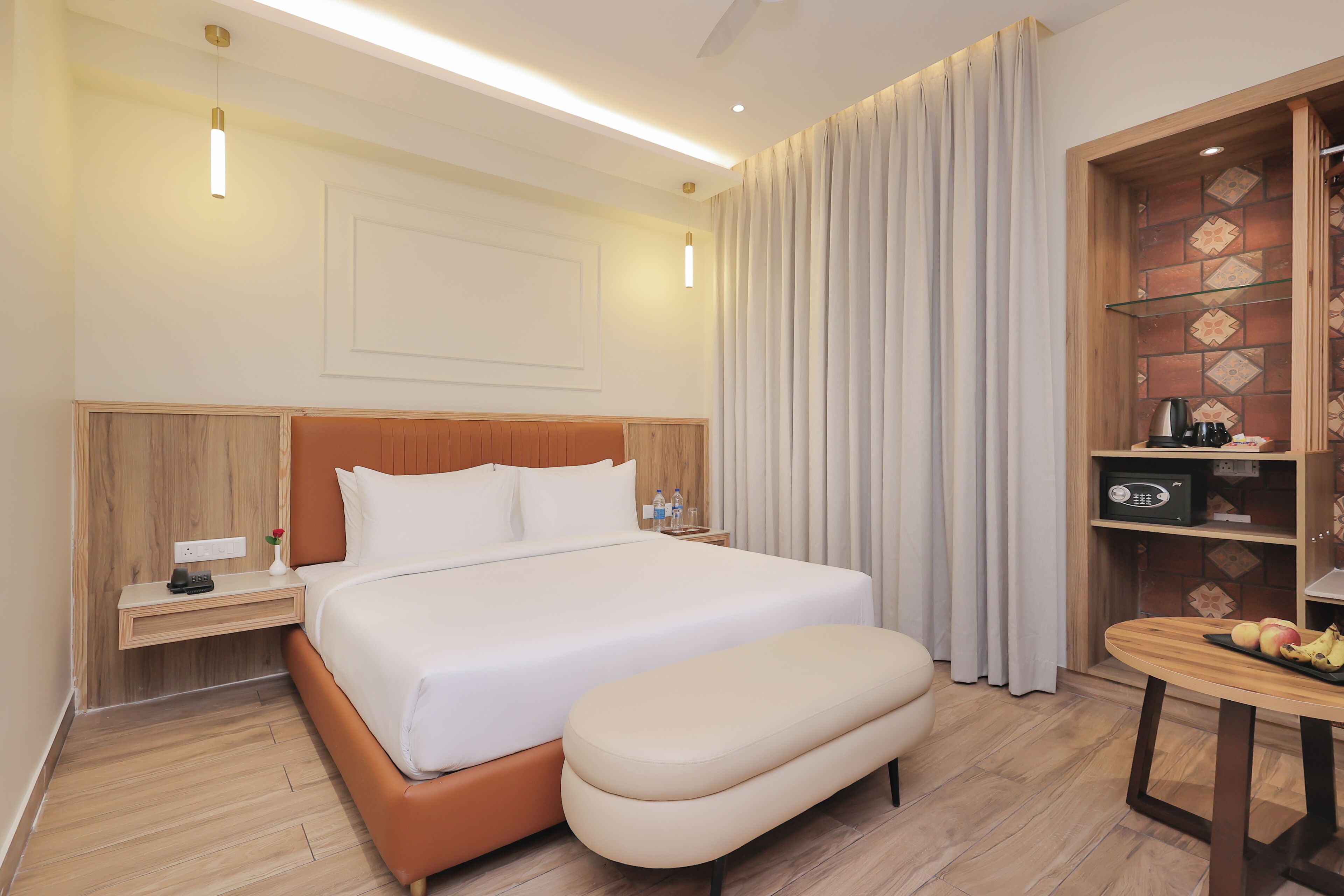 Habitación de hotel con una cama grande, cabecera de madera, mesita de noche con lámpara, una pequeña mesa con frutas y un panel decorativo en la pared.