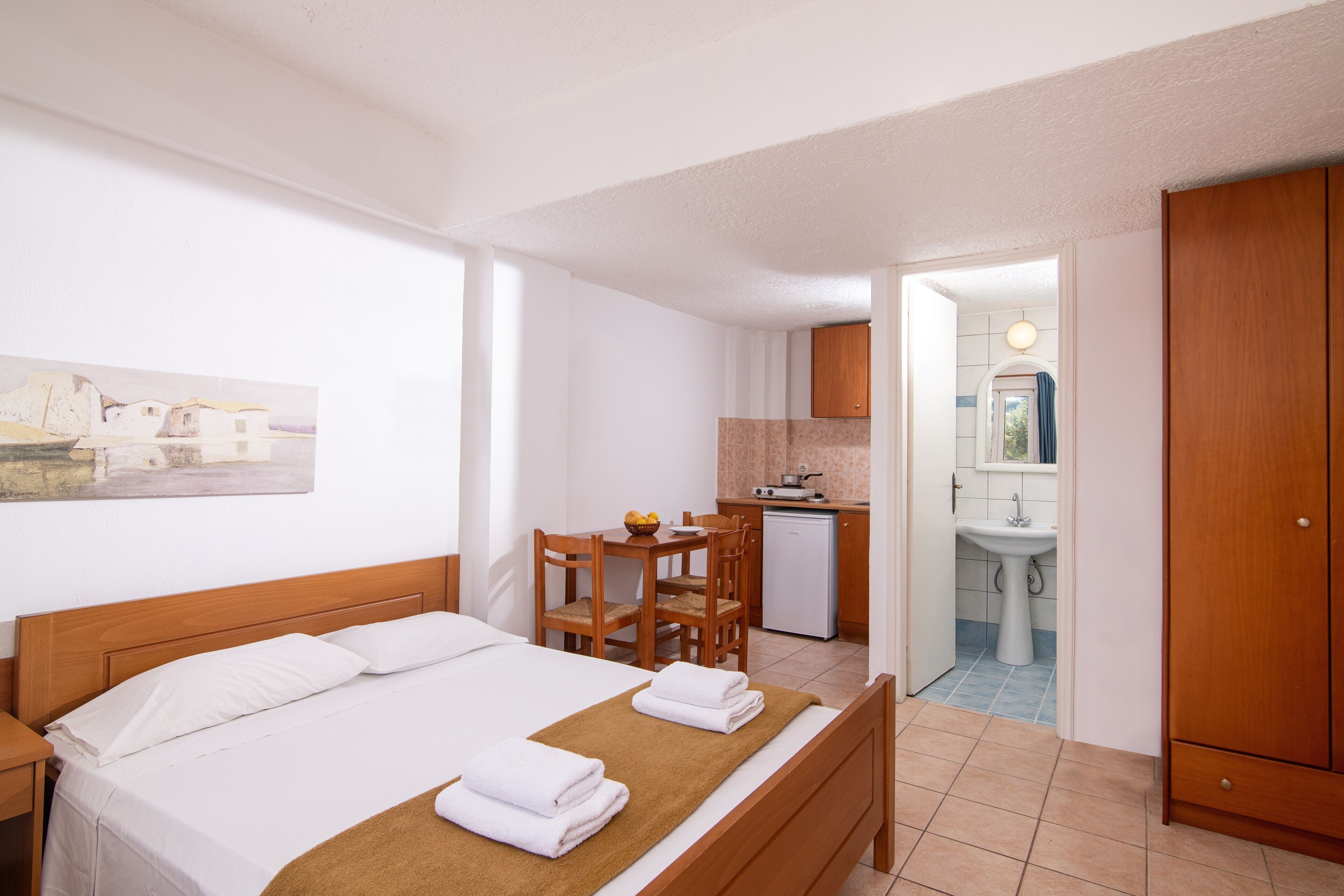 Una habitación de hotel con cama, escritorio de madera, kitchenette pequeño y baño.