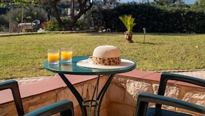A table with two glasses of orange juice, a woven hat, and a potted plant in a garden setting.