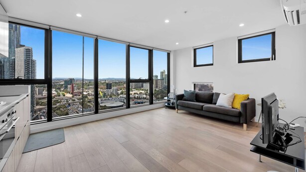 A modern living room with large windows, a grey sofa, and a flat-screen TV. - Amazing city view 2BR Apt Mel CBD Parking (Southbank)