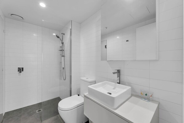 A modern bathroom with a glass-enclosed shower, a white toilet, and a vanity with a sink and mirror.