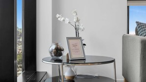 A modern room with a glass table holding a vase with white flowers and a framed sign. - Amazing city view 2BR Apt Mel CBD Parking (Southbank)