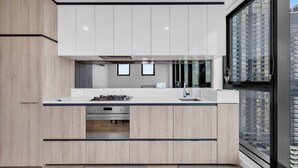 A modern kitchen with white cabinets, a stainless steel stove, and a large window offering a city view. - Amazing city view 2BR Apt Mel CBD Parking (Southbank)