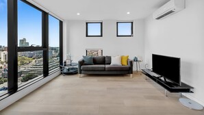 A modern living room with a large window, a sofa, a flat-screen TV, and a small side table. - Amazing city view 2BR Apt Mel CBD Parking (Southbank)