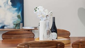 A wooden table with a white vase and a wine bottle, and a painting on the wall.