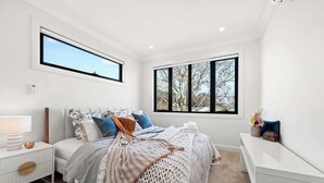 A bedroom with a bed, nightstand, dresser, and large windows.