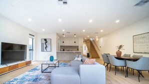 A modern living room with a large TV, a sofa, a coffee table, and a dining area with chairs. - 4BR Brand new Townhouse in Ashburton Shopping Golf (Ashburton)