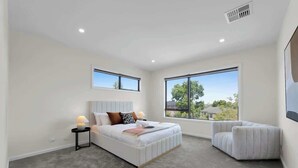 A bedroom with a bed, bedside tables, a chair, large windows, and a ceiling vent. - 4BR Brand new Townhouse in Ashburton Shopping Golf (Ashburton)