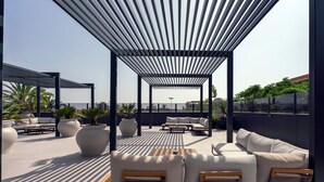 Une terrasse sur le toit dotée d’un espace salon couvert, de grands pots de plantes et d’une vue sur le panorama urbain.