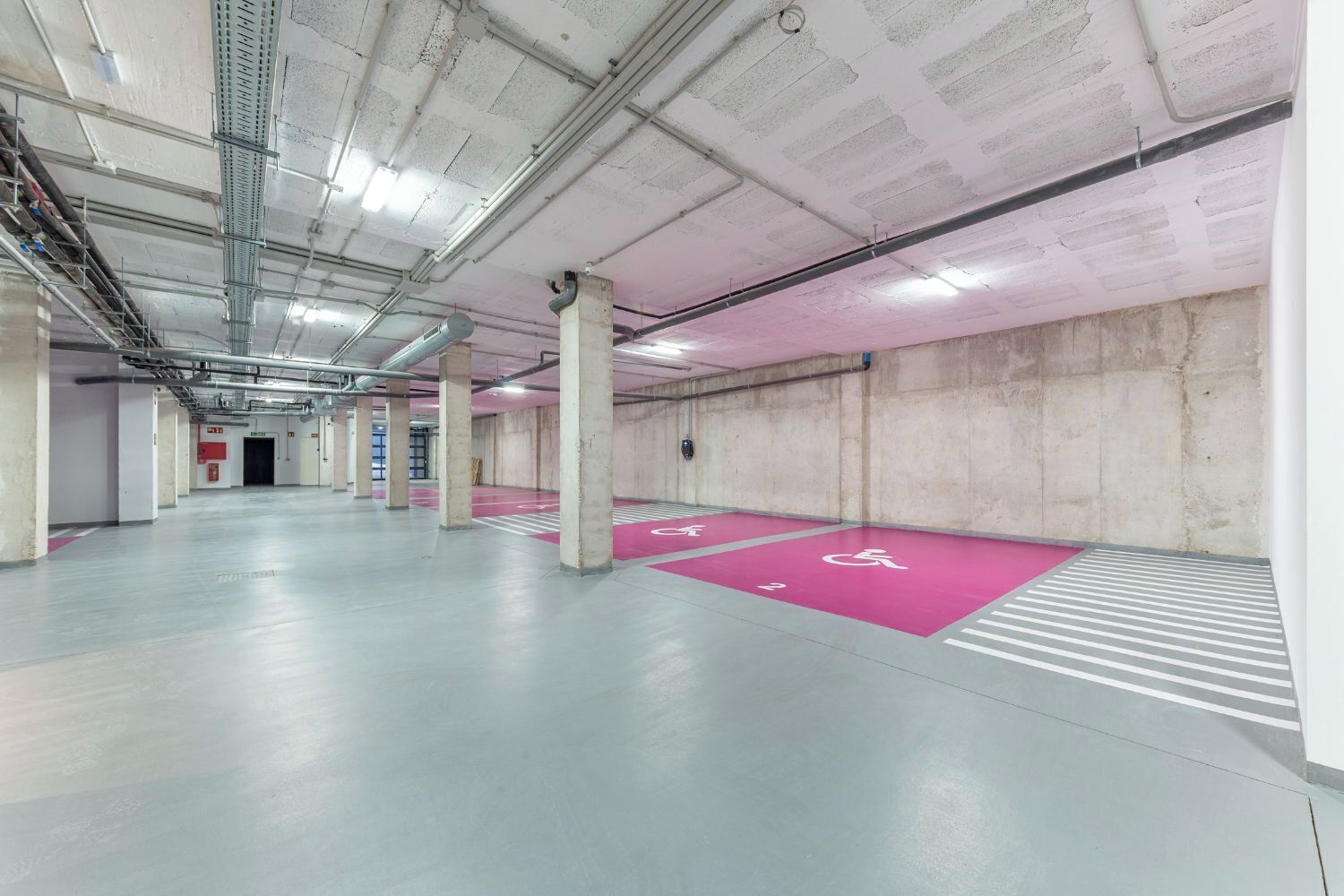 A spacious indoor parking area with concrete pillars, marked parking spaces, and a clear pathway leading to an exit.
