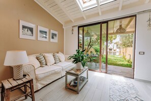 Un salón con un sofá blanco, una mesita de centro y una lámpara. Hay cuadros en la pared y una planta sobre la mesita.