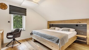 A modern bedroom with a sloped ceiling, a large bed, a desk, and a chair.