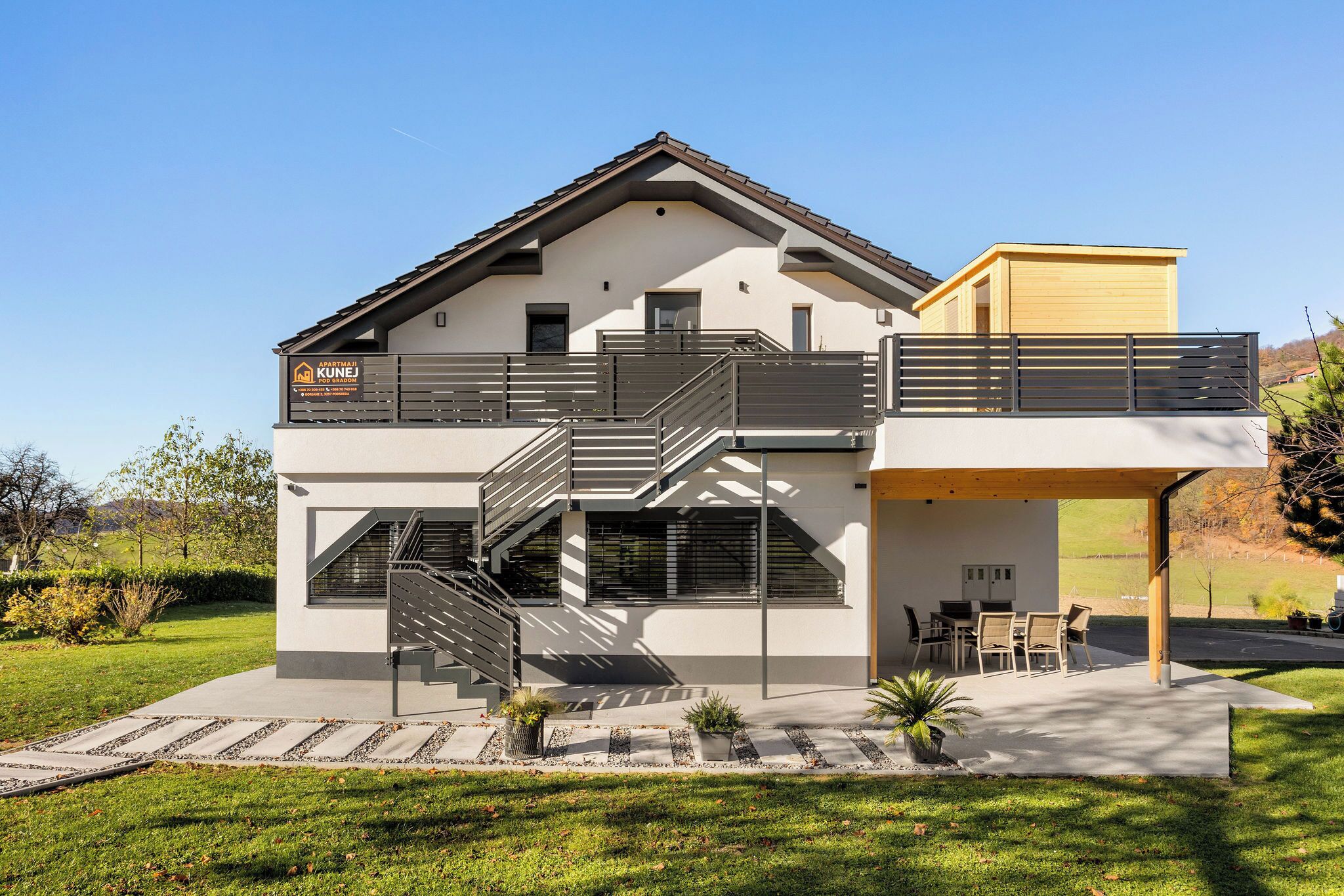 Una casa moderna de dos pisos, con balcón, escalera y zona de estar exterior cubierta.