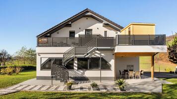 Una casa moderna de dos pisos, con balcón, escalera y zona de estar exterior cubierta.