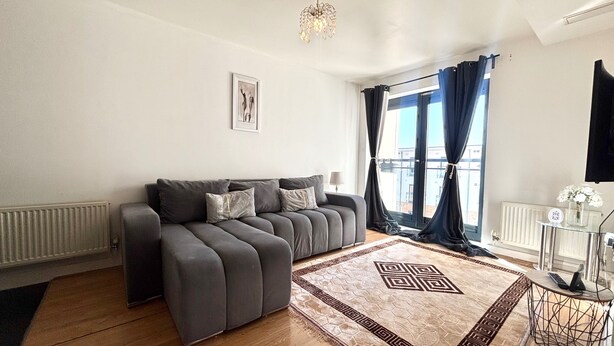 A modern living room with a grey sofa, a patterned rug, a chandelier, and a view through large windows. - 1 Bed Flat - Sleeps 4 - Pets - Parking - Wifi (Grays)