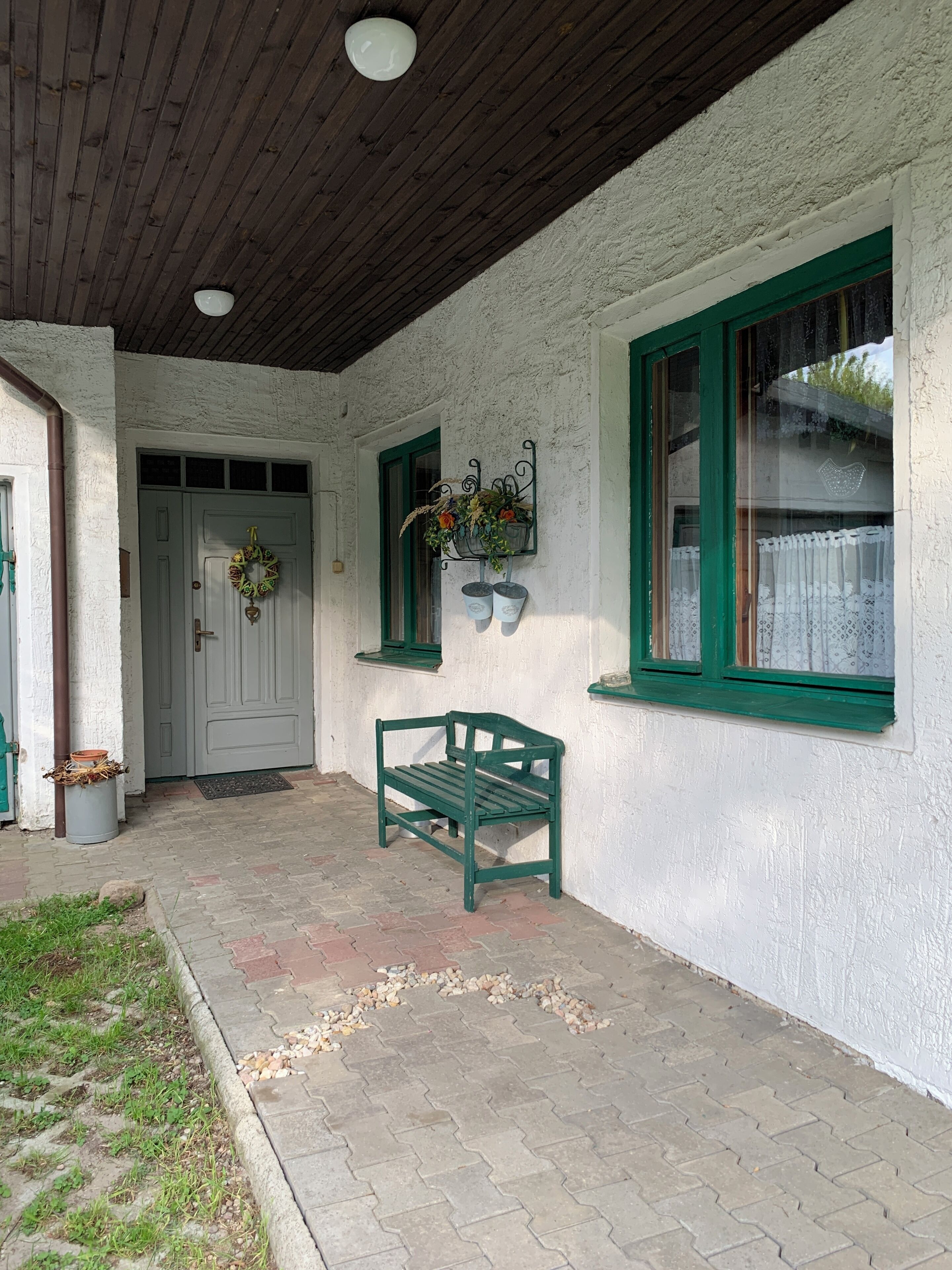 A covered porch with a green bench, a white wall with green trim, and a door with a wreath.