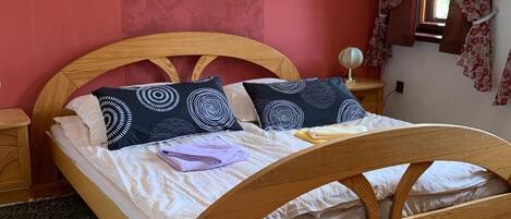 Un dormitorio con estructura de cama de madera, pared roja y ventana con cortinas florales.