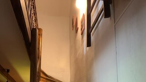 A wooden staircase with a handrail, a light fixture above, and a door at the bottom.