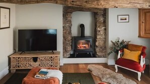 A cozy living room with a stone fireplace, a television on a wooden console, a red armchair, and a lamp. - Boutique Luxury at The Nook (Cockermouth)