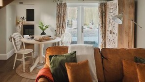 A cozy living room with a brown sofa, a dining table with chairs, and a view through a glass door to an outdoor area. - Boutique Luxury at The Nook (Cockermouth)