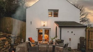 A white house with a stone wall, a wooden fence, and a patio with outdoor furniture. - Boutique Luxury at The Nook (Cockermouth)