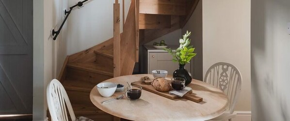 Una mesa redonda de madera con un bol, una taza y una hogaza de pan.