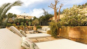A patio area with outdoor seating, including a sofa and chairs, surrounded by potted plants and a large umbrella. - Architect-designed Riad close to the Secret Garden, for rent as a whole with private pool (Marrakech)