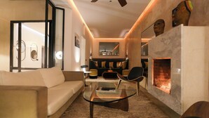 A modern living room with a glass coffee table, a sofa, a fireplace, and a seating area with a chair and a side table. - Architect-designed Riad close to the Secret Garden, for rent as a whole with private pool (Marrakech)